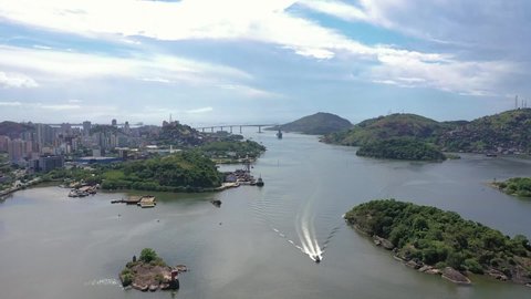 drone aerial panorama of the entire port of Vitoria city overlooking Vitoria city, Vila Velha city, Terceira Ponte bridge, Morro do Moreno hill. with a cargo ship approaching. Sunny day with few cloud