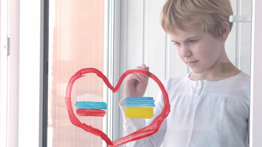 The child dreams of peace. friendship concept. The child draws the flags of Russia and Ukraine on the window. heart shape. The concept of peace and mutual understanding. War 2022. Peace 2022. Reaching