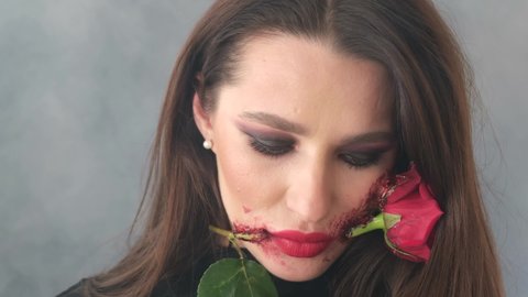 Brunette woman in halloween costume wearing witch makeup with flower in mouth 