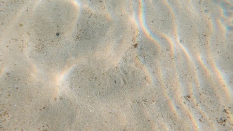 A beautiful top footage of sun rays penetrating clear sea water making up beautiful sun dog pattern with rainbow spectrum glow on sand bottom. Natural sun light texture of undersea background