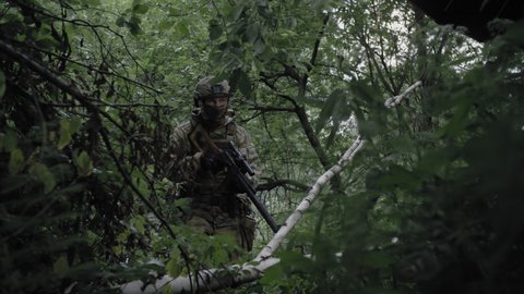 Close-up, an armed soldier with a sniper rifle, in a dense forest, spotting an enemy, aiming through an optical sight. Equipped soldier in action