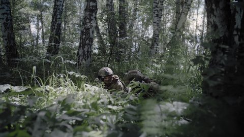 Soldier with sniper rifle on military operation gives command to partner with sniper laser rangefinder. Special forces soldiers work as team protecting the front line while sitting in ambush