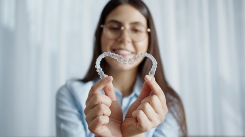 Close-Up Portrait Of A Woman Holding A Plastic Transparent Retainer. A Girl Corrects A Bite With The Help Of An Orthodontic Device, Holding Two Transparent Heart-Shaped Aligners, Invisalign Braces