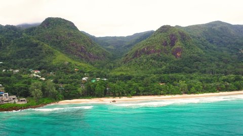 Flying from Grand Anse Beach at the Mahe Island, Seychelles, with turquoise water of the Indian Ocean, mountains and rain forests in the background.