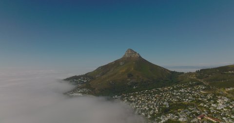 Aerial panoramic shot of Lions Head mountain towering above residential neighbourhood and sea coast covered with dense fog. Cape Town, South Africa