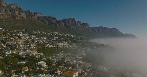 Static shot of touristic resort at seacoast with high rocky escarpment in background. Morning fog rising from water surface. Cape Town, South Africa