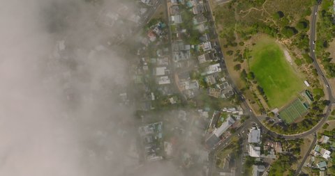 Fly above coastal city, limited visibility due fog rising from sea. Houses, streets and sports areas in urban neighbourhood. Cape Town, South Africa