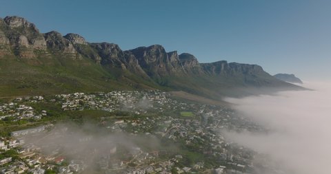 Descending shot of rock escarpment above tourist destination. Fog rising from sea. Cape Town, South Africa