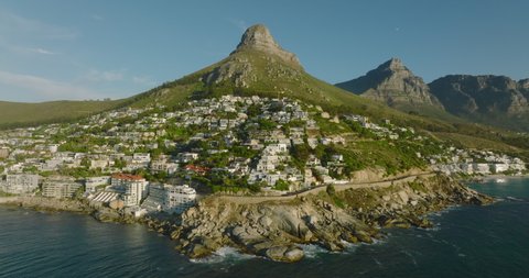 Luxury residential borough under high mountain lit by bright sunshine. Backwards revealing of sea coast. Cape Town, South Africa