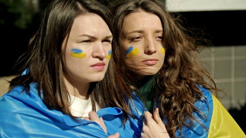 Women with the flag of Ukraine on their shoulders, looking into the distance with excitement and hope. Protest against the war in Ukraine and Russian aggression.