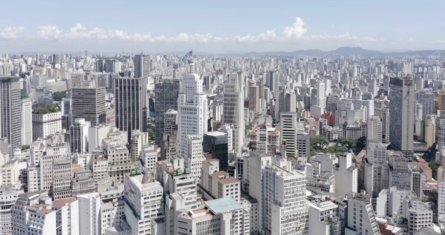 side drone flight over downtown Sao Paulo, state flag fluttering on top of a building, blue sky, Sao Paulo, Brazil