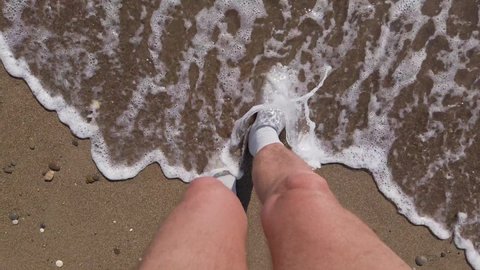 Male feet in socks. The point of view of a man walking on wet sand in socks. Walk on the waves in socks. Very strange behavior concept.