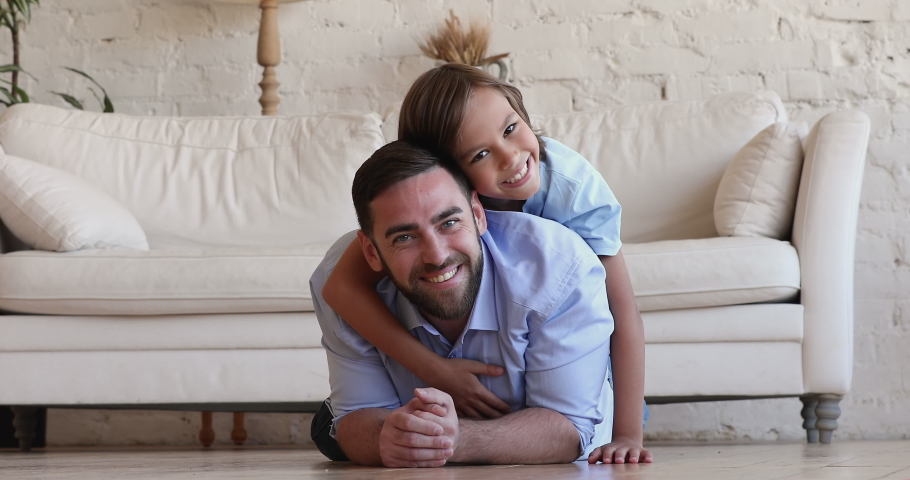 Overjoyed handsome father and preteen son portrait. 10s lovely boy piggyback his loving daddy, lying together on warm floor in cozy living room smile look at camera. Cherish, family ties, bond concept Royalty-Free Stock Footage #1088401185