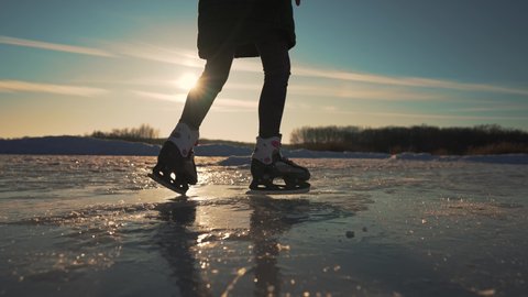 The child is skating on ice. Ice lake in the park. skater on frozen ice. Winter nature at sunset. Pond outdoors in the park. Happy child is skating on the ice in the park. Winter outdoor games
