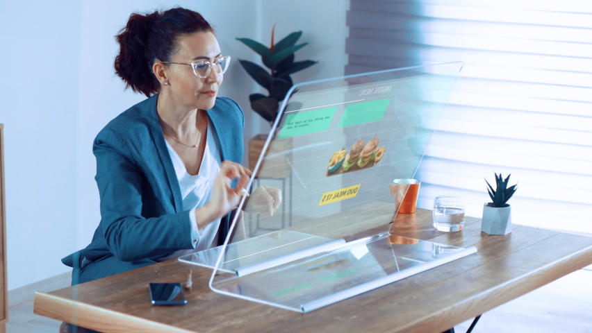 Woman orders food home in online store using a computer with transparent display. Excited woman picking fast food online | Shutterstock HD Video #1088402463