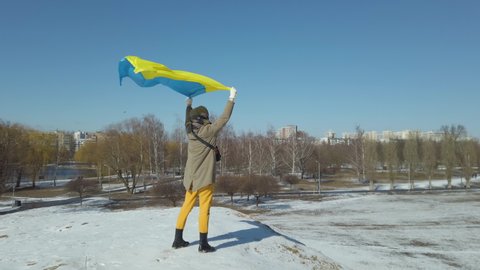 War in Ukraine, Young woman holding national flag of Ukraine over her head during russian occupation. Support, Save, Help, Pray for Ukraine. 