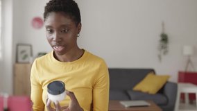 Female blogger recording a video while sitting in the living room at home. Young african woman having fun while vlogging about beauty products on social media network - High quality 4k footage