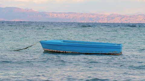 Empty blue boat is rocking on Red sea waves. Fishing old boat swaying on ripple water surface in windy day. Motor ship, outboard runabout floating near seaside. Travel, tourism, fishery