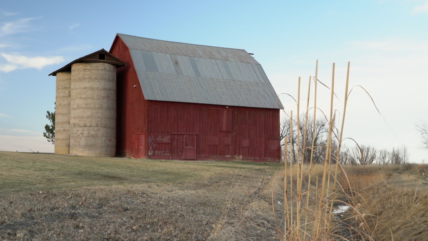 old red barn with twin silo and irrigation ditch at Colorado foothills, winter or early spring scenery with reeds moved by a breeze