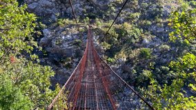 Point of view video. Slowmotion shot of a person walking along old metal rope bridge across the Moraca river canyon in Montenegro