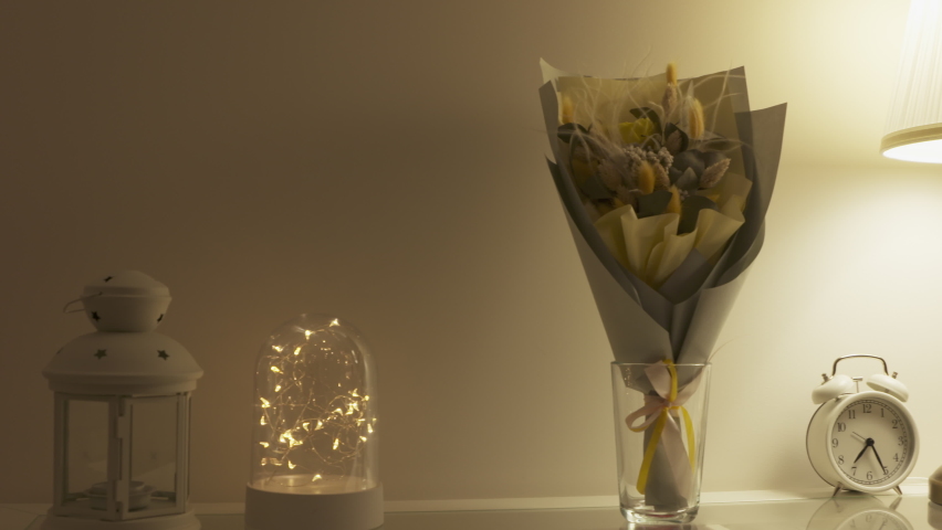 Console table with bouquet of flowers lit by a table lamp in the living room, apartment decoration background. High quality 4k footage