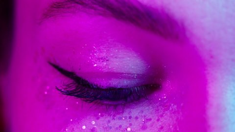 Close-up of young woman eye wearing decorative lenses in ultraviolet light, makeup with glitter and eyeliners. Advertising of protective contact colorful lenses for performances, halloween.