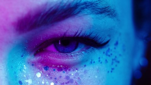 Close-up of young woman eye wearing decorative lenses in ultraviolet light, makeup with glitter and eyeliners. Advertising of protective contact colorful lenses for performances, halloween.