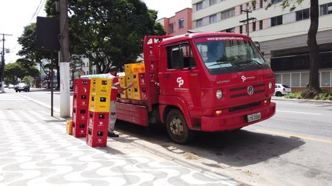 Teresopolis, RJ, Brazil - March 18th 2022 - Beer truck from Grupo Petropolis and Cerveja Itaipava delivering beer boxes. Red and yellow boxes. A male worker moveing the boxes to deliver beer.