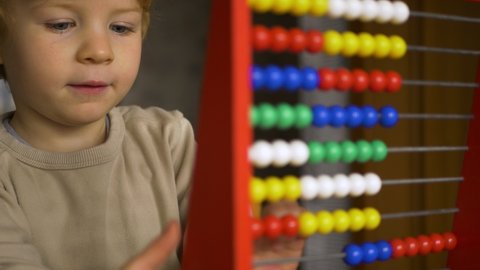 Young blond caucasian boy early learning counting on abacus.