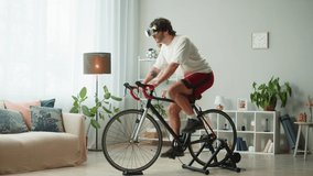 Sportsman riding bicycle, wearing virtual reality glasses, home gym. Young man cycling in living room, exercising in morning. Spanish guy working out on stationary bike. Healthy lifestyle. - Powered by Shutterstock - Get 15% off with code: PIKWIZARD15