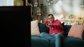 Asian man watching television. Young Korean guy changing channels on tv, using remote control, sitting on sofa in living room, male person relaxing at home, watch film. - Powered by Shutterstock - Get 15% off with code: PIKWIZARD15