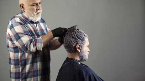 Process of a guy having hair dyed at hairdresser salon. Bearded man coloring hair. Hipster bearded men dye his hair color on a gray background.