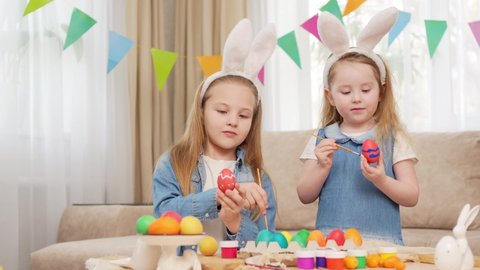 happy sweet little girls with rabbit ears celebrate Easter and decorate eggs with paints. Easter Bunny. the tradition of decorating eggs and cooking traditional treats with the whole family.