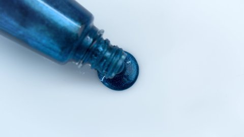 Blue mother-of-pearl glitter nail polish flows out of an overturned bottle. Advertising concept for decorative cosmetics.
