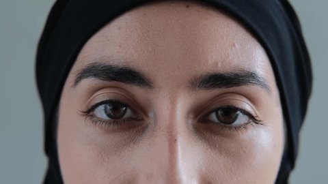 Close-up of brown eyes with black eyebrows look into the frame so deeply that they look into your soul. A Muslim woman with a cruel look pierces with her gaze. Arabic culture.