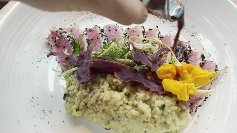 Delicious tuna tataki with edible flower and rice. Male hand pouring soy sauce on raw fish with sesame and spices on a plate in luxurious restaurant. Healthy lunch of asian cuisine.