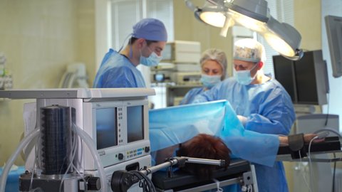 KYIV, UKRAINE - August 2021: Anesthesia machine with a moving ventilation pupm at foreground. Surgeons team performing operation at backdrop in blur.