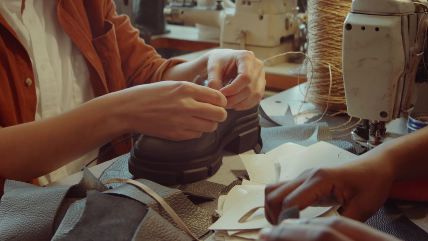 Caucasian and African American female colleagues chatting while working together in shoemaking workshop