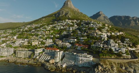 Slide and pan shot of luxurious apartments in steep slope at sea coast. Mountains in background. Cape Town, South Africa