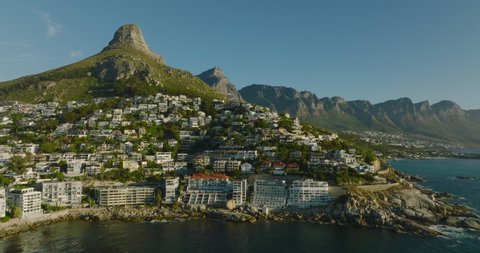 Fly around sea coast lined by luxury properties and hotels. Rock mountain ridge in background. Cape Town, South Africa