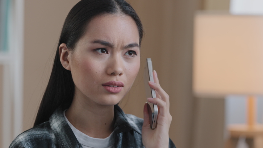 Portrait asian woman millennial confused angry girl indoors talking on phone answering call worries about bad mobile connection network problems cellular trouble broken smartphone breaking telephone | Shutterstock HD Video #1088430595