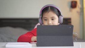 asian child smile learning on computer tablet or kid girl student back to school and wearing headset for video call listening studying or person enjoy learn from home by study online class in bedroom