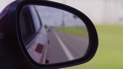 View in the side rear view mirror of a car driving a red car on a highway