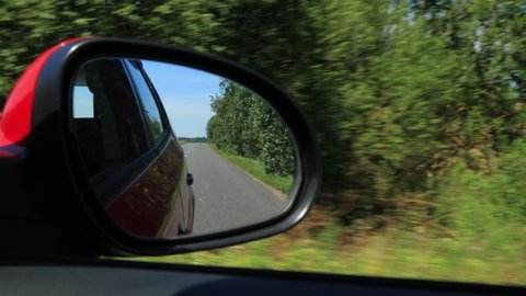 View in the side rear view mirror of a car driving a red car on a highway