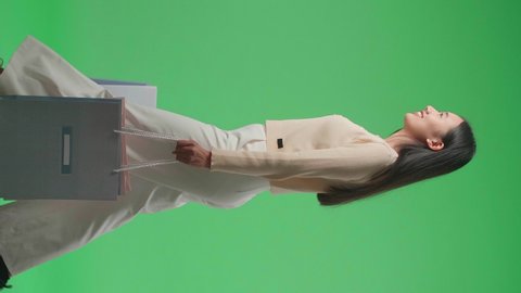 Side View Of An Asian Shopping Woman With Shopping Bags Smile And Walking In Front Of Green Screen
