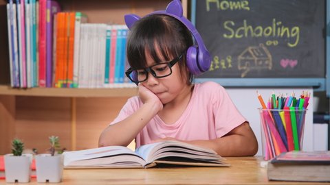 Cute little girl with headphones listening to audiobooks and looking at English learning books on the table. Learning English and modern education