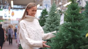 Christmas shopping. Woman choose artificial Christmas tree touching her on traditional Christmas market. Caucasian female looking looking for perfect xmas tree to buy on the tree shop. Happy holiday  - Powered by Shutterstock - Get 15% off with code: PIKWIZARD15