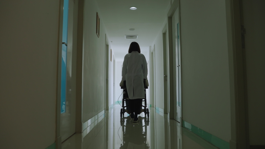 Asian female doctor is talking and pushing a wheelchair to patients down a hospital corridor.
 Royalty-Free Stock Footage #1088442259