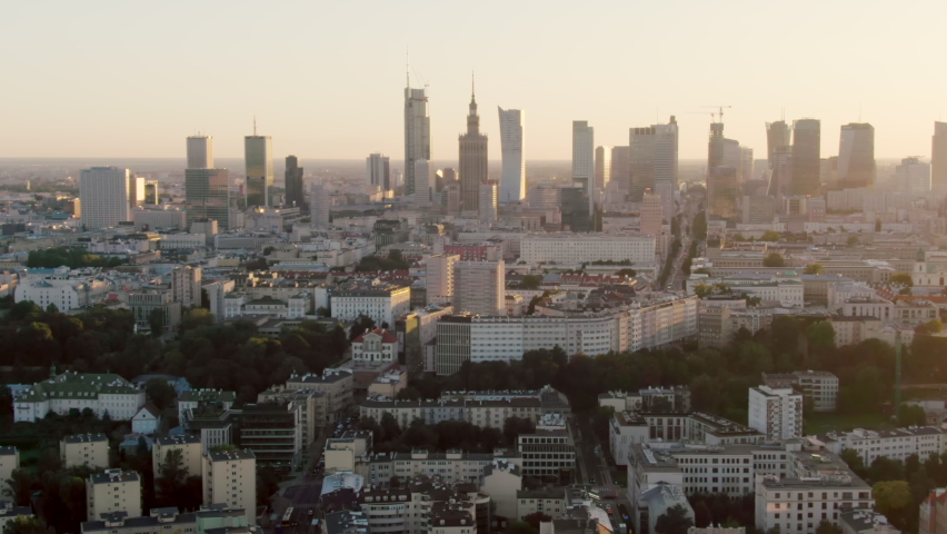 Establishing Aerial Panorama of Warsaw City Skyline - Capital of Poland, Europe. Modern Downtown Urban Cityscape on Sunset with Golden Sky. 4K scenic drone zoom in shot