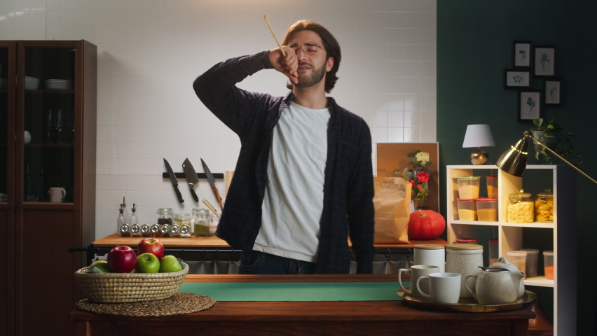 Spanish man chef dancing and singing in kitchen. Young husband having fun. Cooking family dinner and playing. Cheerful happy latin american guy listening to music.